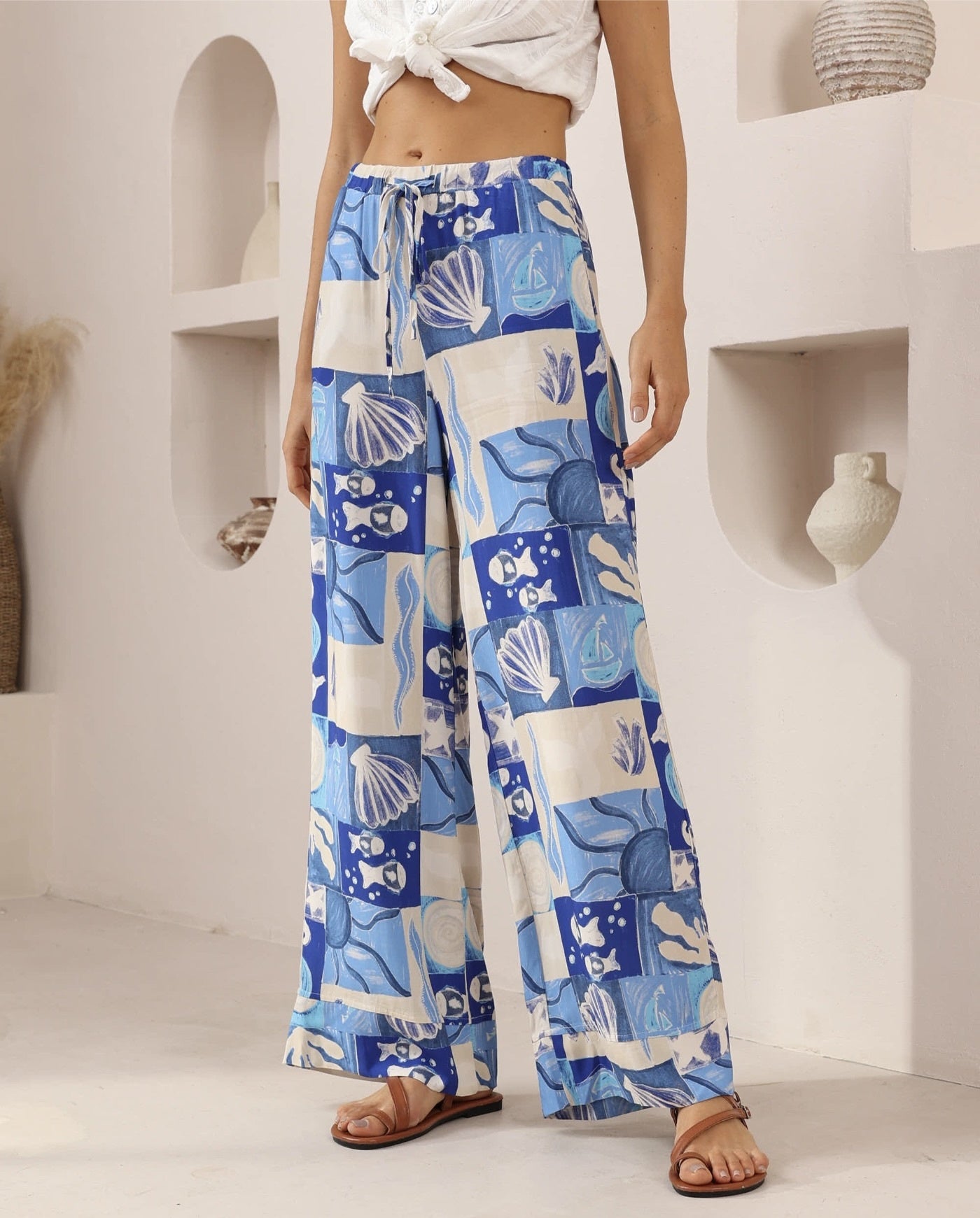 Person wearing blue and white patterned pants with a white top in a minimalistic setting.