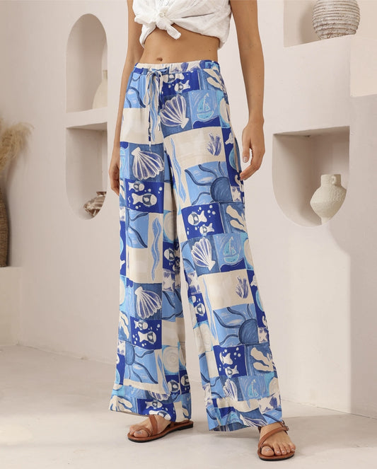 Person wearing blue and white patterned pants with a white top in a minimalistic setting.