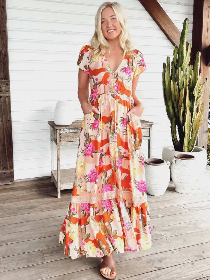 Experience the effortless elegance of the Carmen Maxi Dress. Designed with a classic V-neckline, short sleeves, elasticated waist, and buttons full length, this stylish dress boasts two pockets for a touch of luxury. The traditional Agave print is the perfect finishing touch, creating a timeless look that will turn heads.